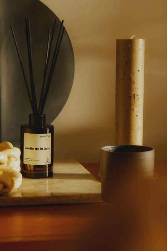 A diffuser bottle labeled 'Jardin de la Lune' on a wooden surface with a candle and decorative elements.