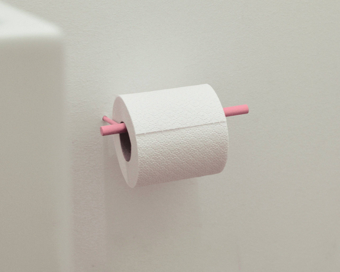 A roll of white toilet paper mounted on a light beige wall, with a pink holder or rod visible on both sides.