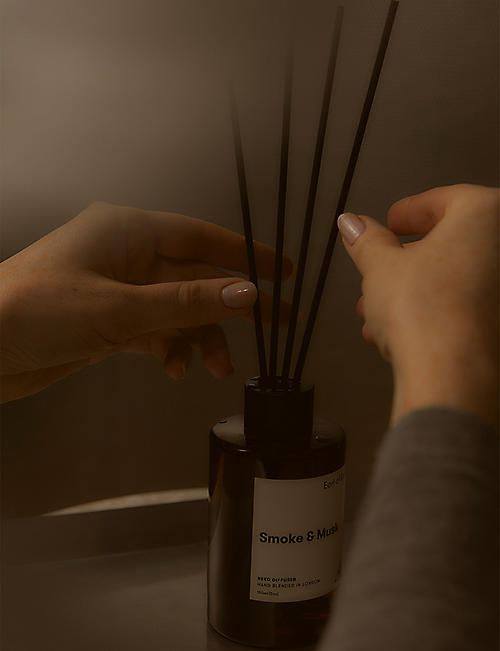 Person holding a diffuser with 'Smoke & Musk' label against a neutral background